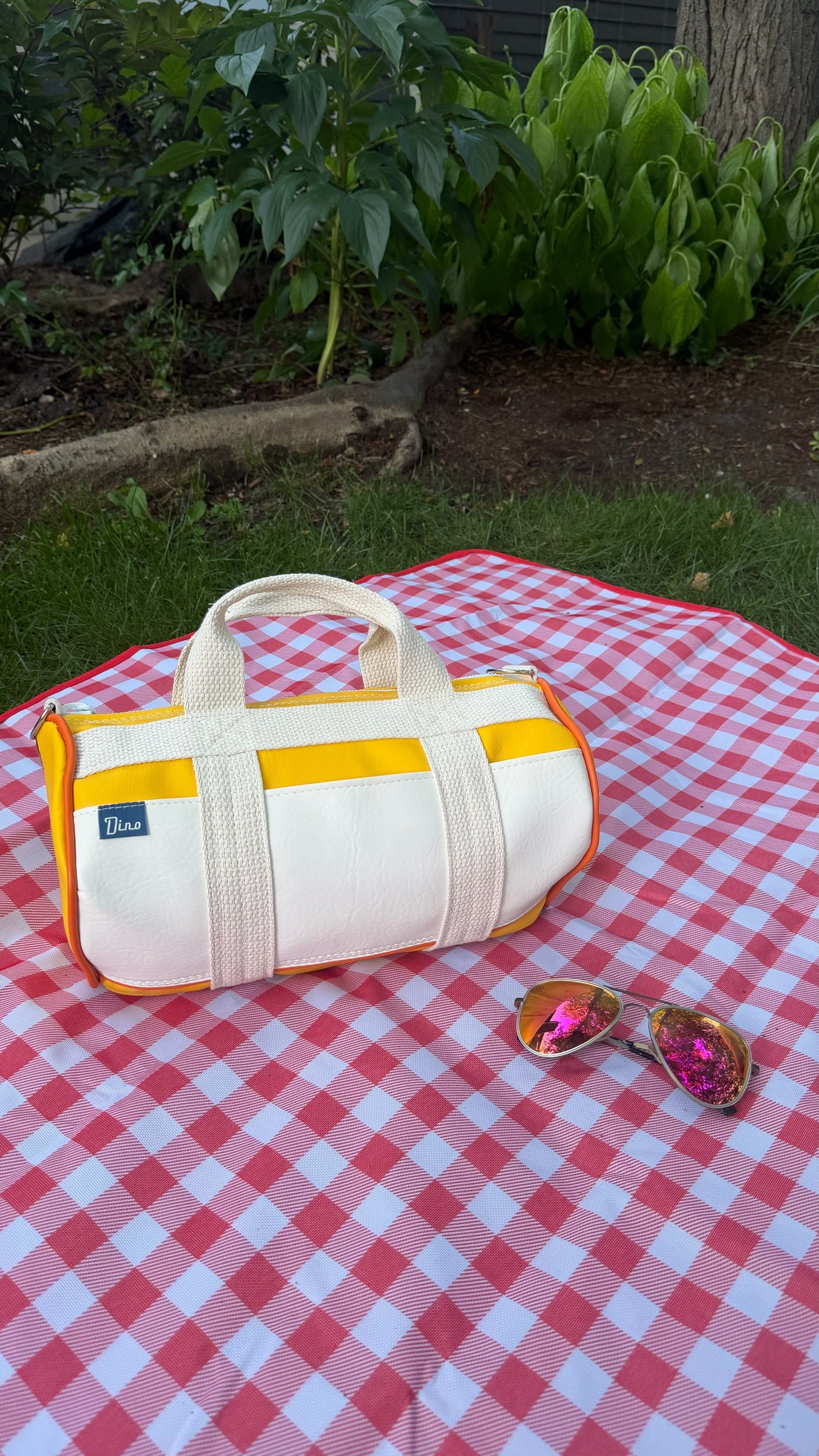 Sunburst barrel duffel on gingham picnic blanket with sunglasses beside it